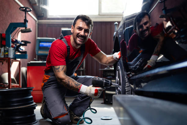 Experienced car mechanic using impact wrench tools and demounting wheels from the vehicle.
